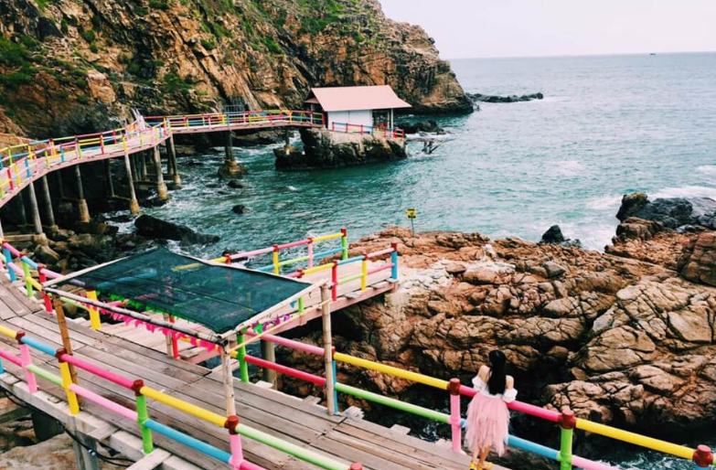 Cầu gỗ uốn quanh vách đá ven biển Eo Gió, nhiều du khách chụp ảnh check-in.