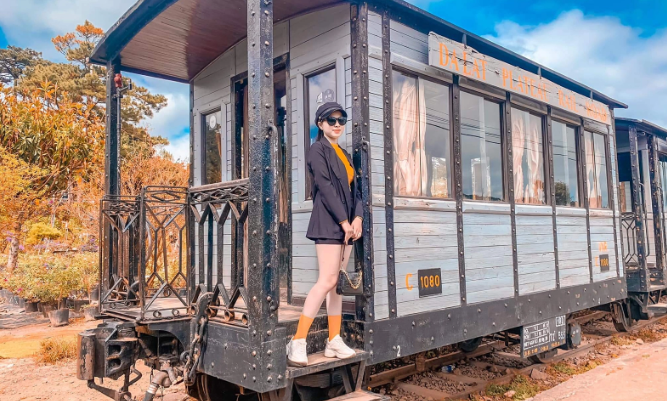 Du khách tạo dáng chụp ảnh trước toa tàu gỗ cũ trong khuôn viên ga Đà Lạt.