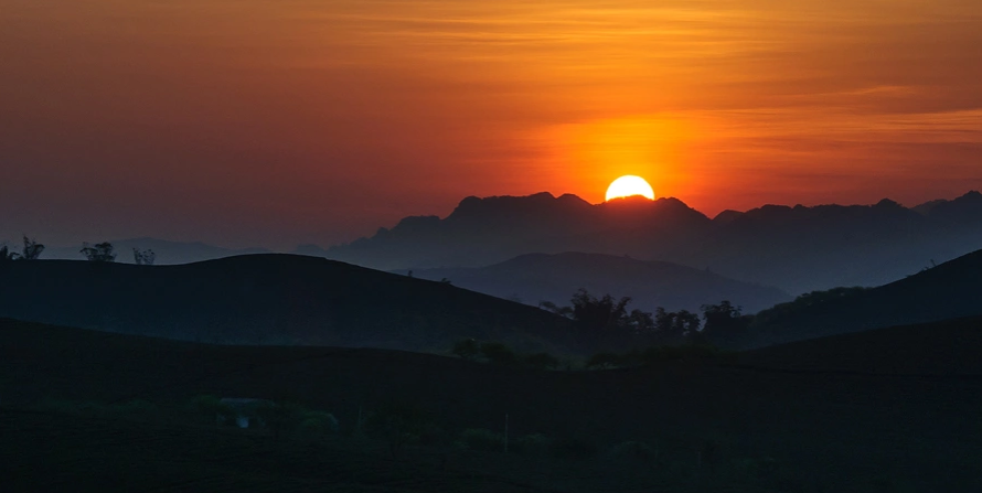 Cảnh mặt trời dần lặn sau dãy núi, bầu trời chuyển cam và tím dịu.