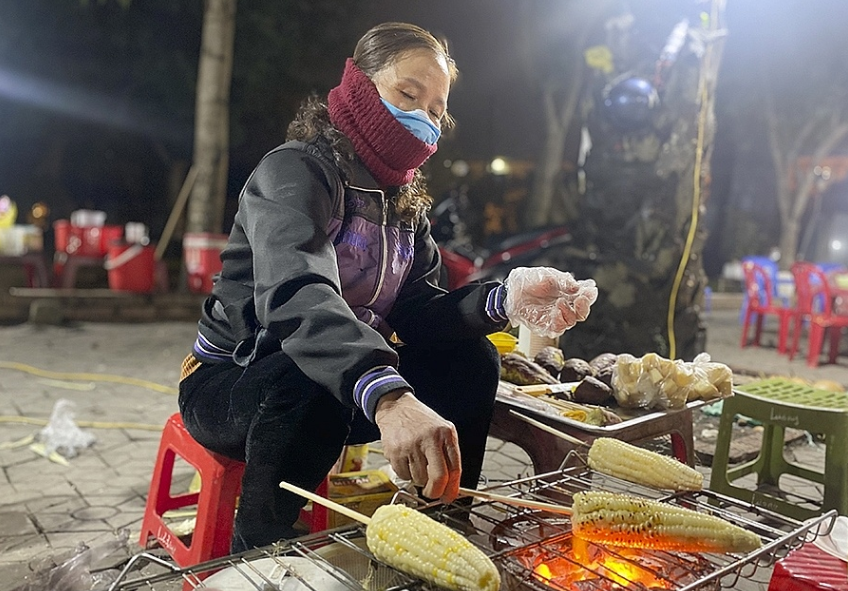 Ảnh người bán ngô khoai nướng trên vỉa hè trong không khí lạnh về đêm.