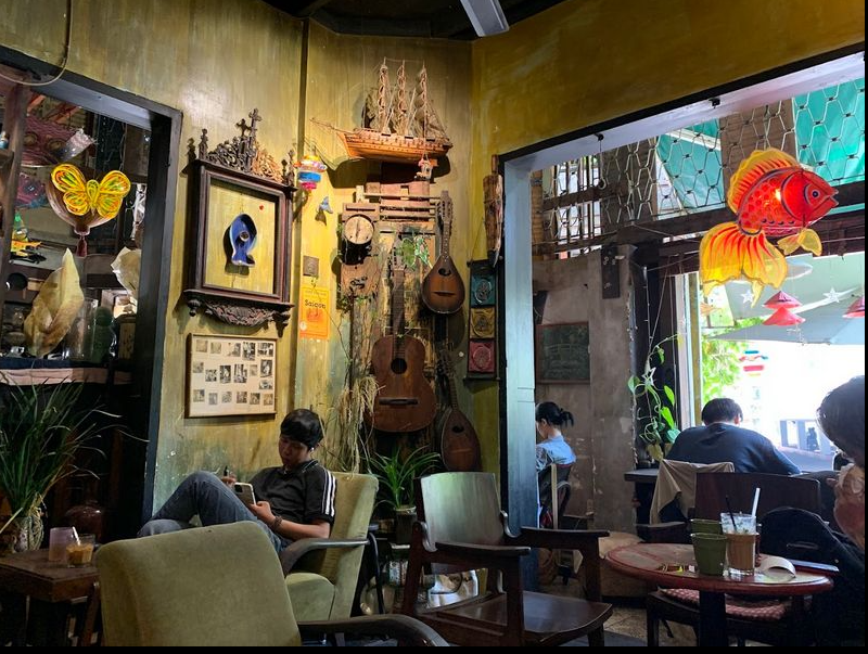 Ảnh chiếc radio cũ, ly cà phê và quyển sổ thơ đặt trên bàn gỗ cạnh cửa sổ ngày mưa.