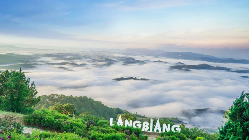 Toàn cảnh núi Langbiang nhìn từ xa với mây bao phủ đỉnh núi, trời trong xanh, cỏ xanh bạt ngàn.