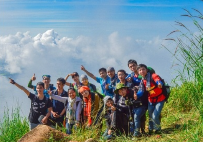 Du khách đứng trên đỉnh Langbiang dang tay đón gió, phía xa là toàn cảnh thành phố Đà Lạt mờ sương.