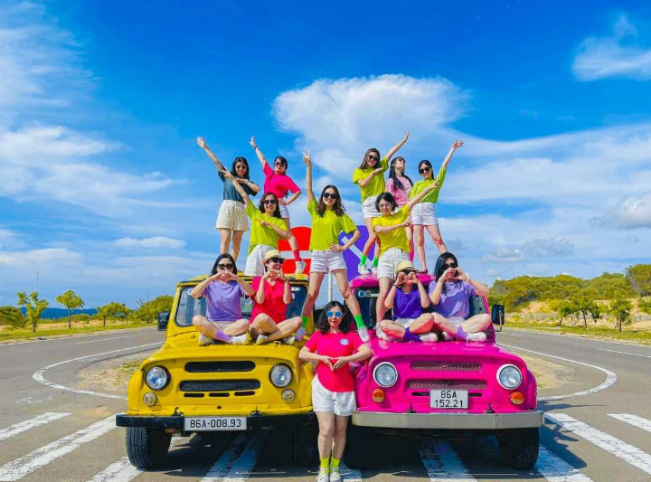 Xe jeep nhiều màu sắc đỗ trên sườn núi, du khách chuẩn bị trải nghiệm dù lượn.