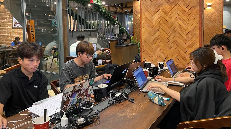 Không gian quán cà phê có khu vực làm việc, laptop, ổ cắm điện và ánh sáng tự nhiên.