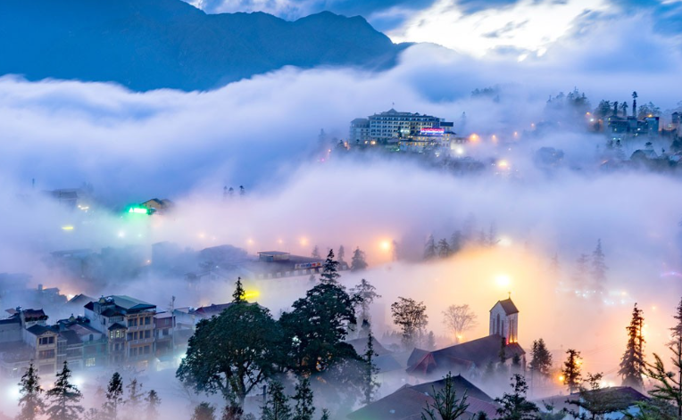 Sương mù bao phủ thị trấn Sa Pa, nhà cửa và rừng thông ẩn hiện trong làn trắng xóa.