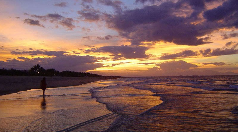 Một du khách đi dạo trên bãi biển Mỹ An vắng lặng trong làn sương mờ buổi sáng.