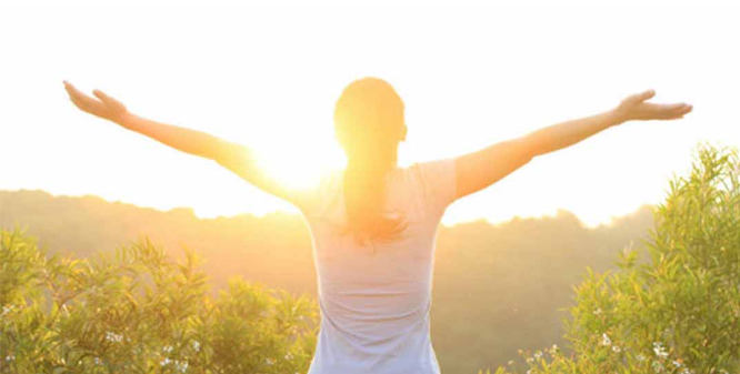 Người đứng dưới nắng buổi sáng nhẹ, giơ tay đón ánh mặt trời để hấp thụ vitamin D.